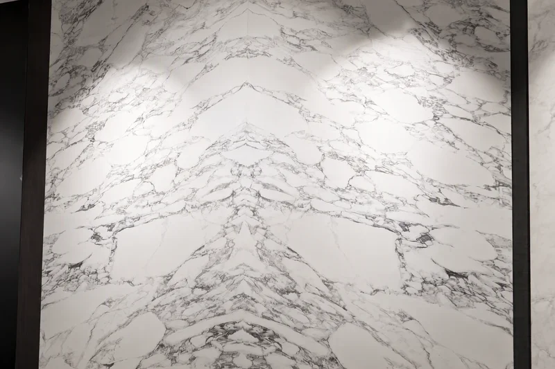White marble-look wall panel with book-matched veining under showroom spotlights
