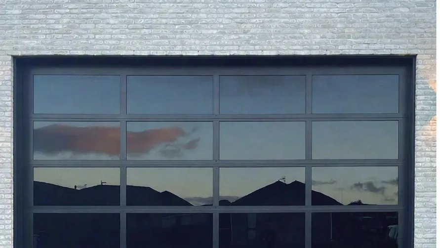 Glass-panel aluminium garage door set into a brick wall